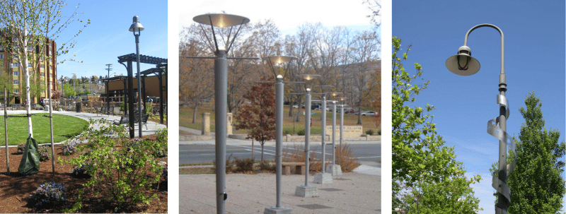 A set of three pedestrian lighting options along different pathways. They are all made of metal, two are topped with lights and the third has a bend in it so the light is pointing down. 
